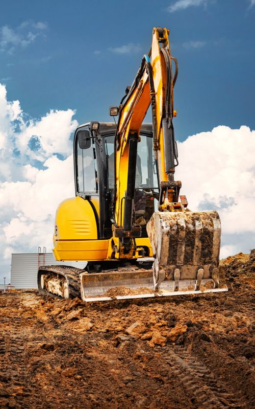 Mini excavator at the construction site on the edge of a pit against a cloudy blue sky. Compact construction equipment for earthworks. An indispensable assistant for earthworks
